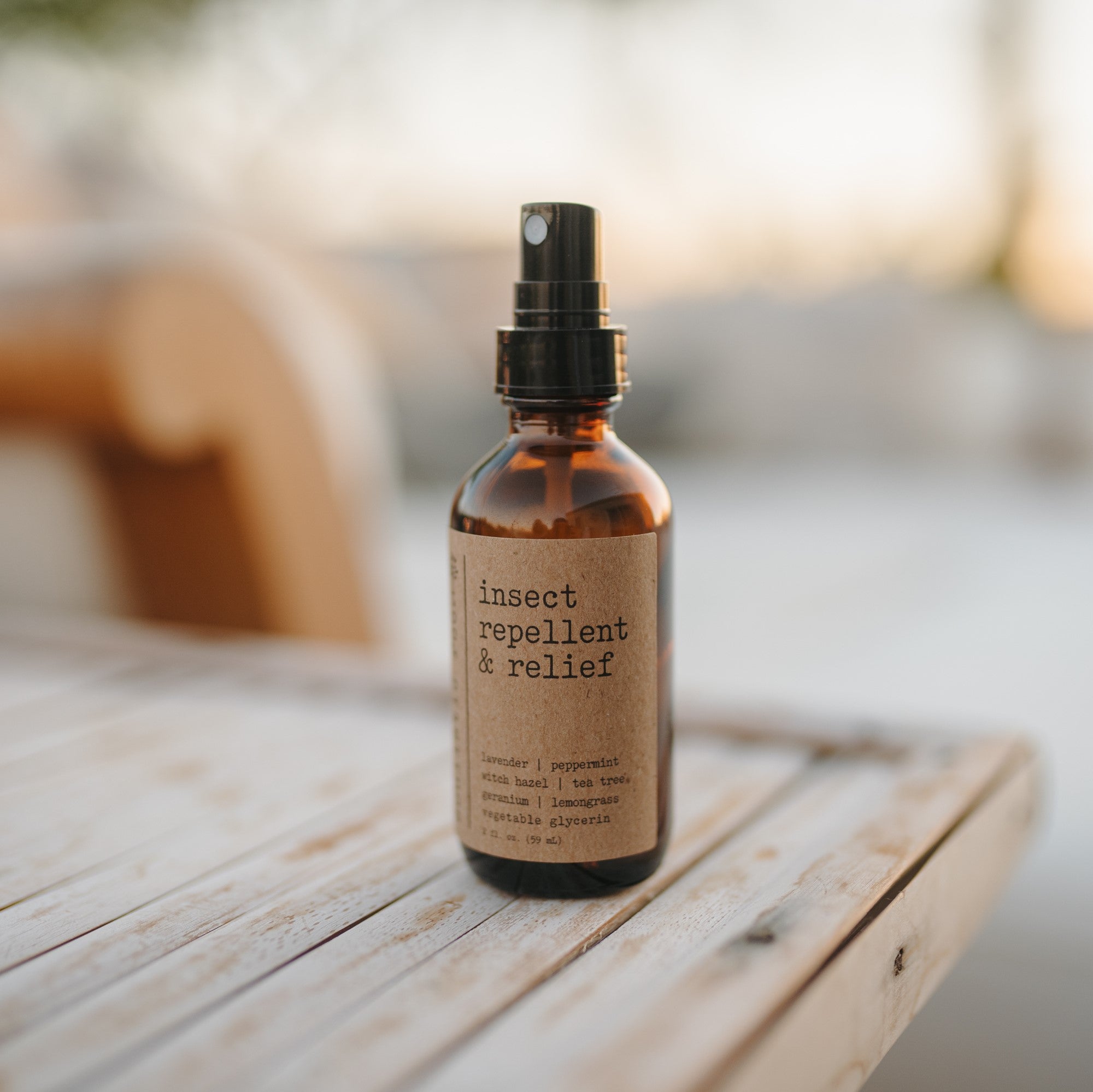 Natural bug spray & bug bite relief 2 oz amber spray bottle sitting outside on a wooden lounge chair