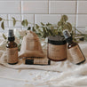 The spa gift set which includes a eucalyptus shower spray, organic lavender oatmeal bath soak, headache relief roller, essential oil & herb revive bath soak and a relaxing pillow mist. The set is on a blanket in front of subway tile and eucalyptus.