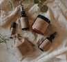 The spa gift set which includes a eucalyptus shower spray, organic lavender oatmeal bath soak, headache relief roller, essential oil & herb revive bath soak and a relaxing pillow mist. The set is on a blanket in front of eucalyptus.