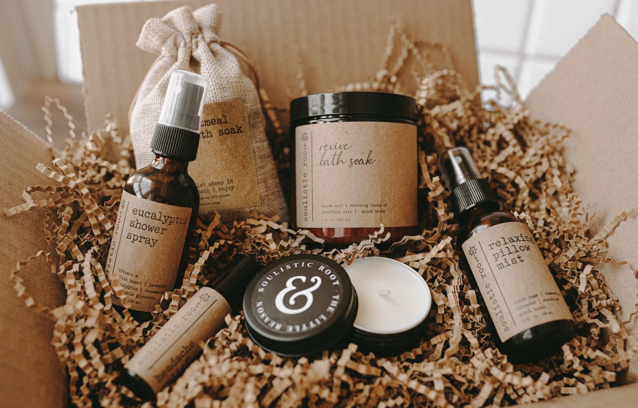 The spa gift set which includes a eucalyptus shower spray, organic lavender oatmeal bath soak, headache relief roller, essential oil & herb revive bath soak and a relaxing pillow mist. The set is in a shipping box with kraft paper and a 1 oz candle that is in a black tin.