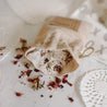 Herbal organic oatmeal bath soak in a burlap bag with some of the contents dumped out showing the oatmeal and rose petals.