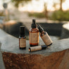 Group shot of natural products on a stone hot springs tub. Products include after sun, bug spray, allergy relief essential oil roller and sore muscle rub