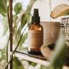 Relaxing essential oil pillow mist in a 4 oz amber glass bottle on a shelf with lots of plants.
